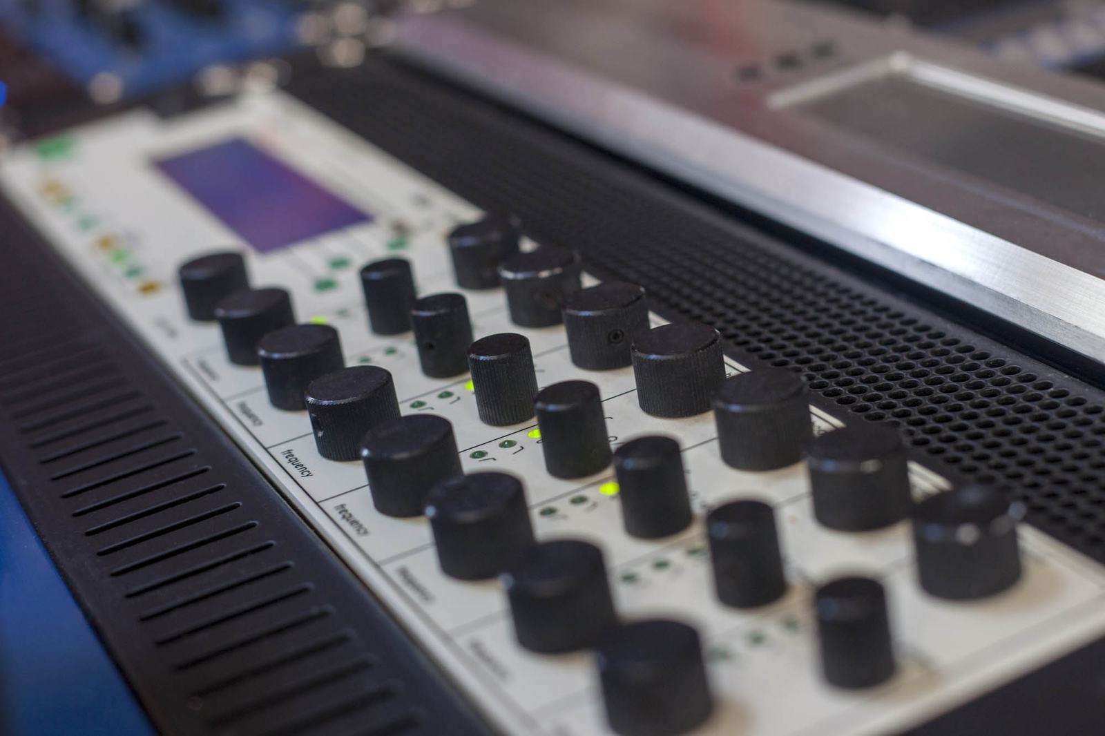 Close-up of a digital mastering processor with black knobs, a small display and a silver front panel